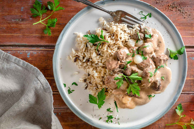 Assiette de blanquette de veau fondant dans une sauce crémeuse avec champignons et oignons perlés servi avec un riz sauvage mélangé.